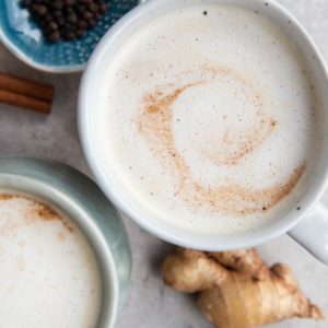 Two chai lattes on a table with spices all around, ready to drink.