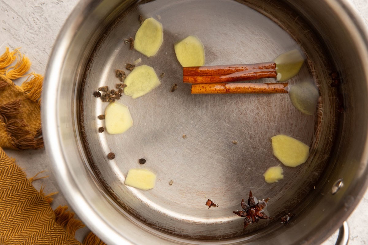 Small pot of room temperature water and spices like cinnamon sticks and fresh ginger.