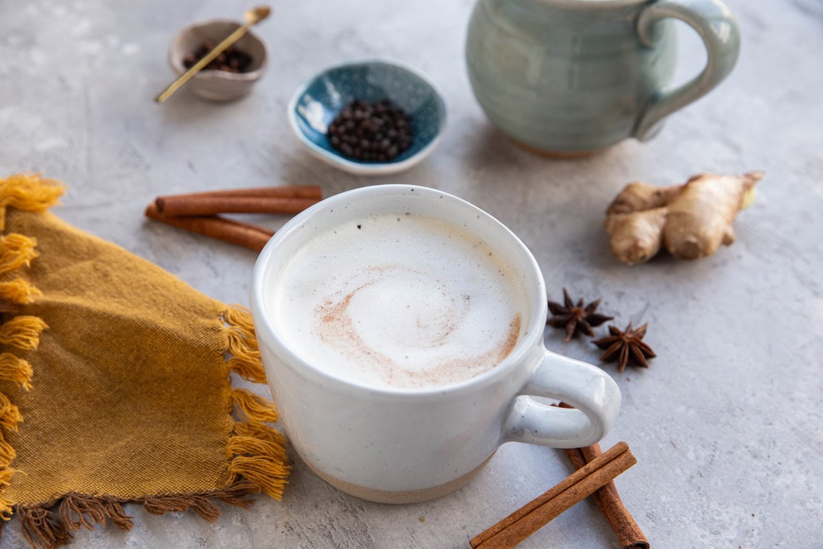 Chai tea latte with chai spices around and another latte in the background with a napkin.