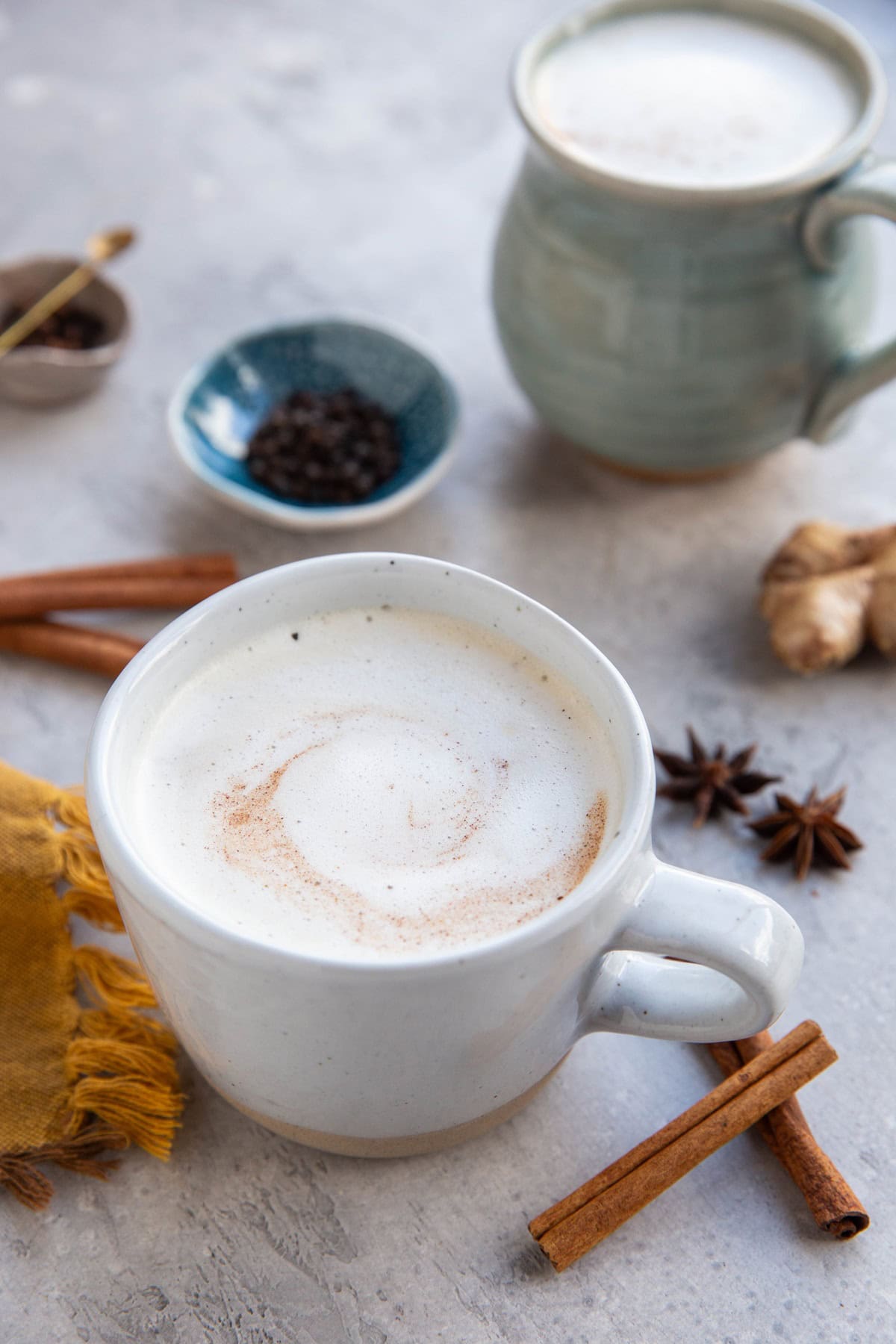 Two mugs of chai tea with authentic Indian spices around and a golden napkin, ready to drink.