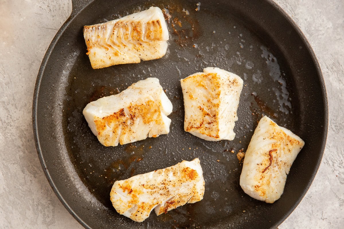 Seared cod filets in a large skillet.