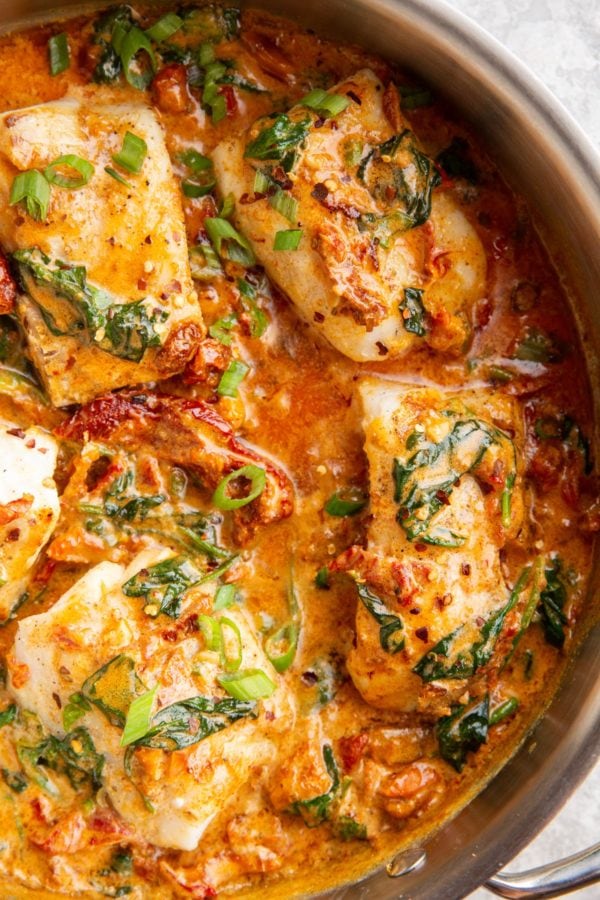 Large skillet full of fish filets covered in creamy sun-dried tomato sauce.