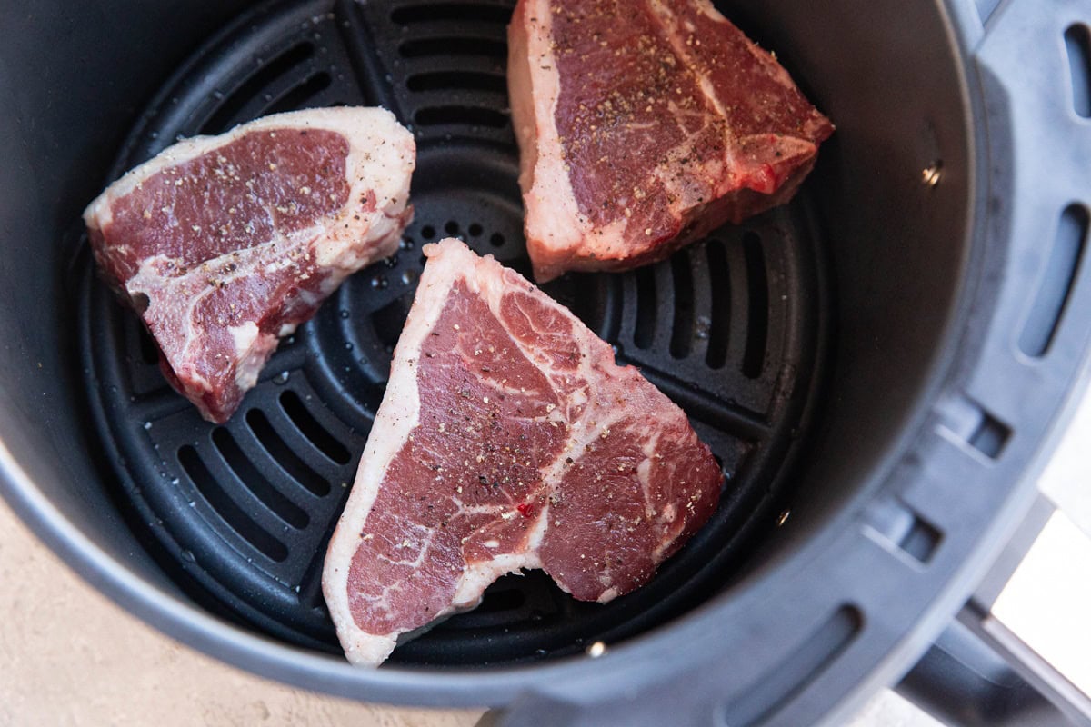 Seasoned pork chops in an air fryer, ready to be cooked.