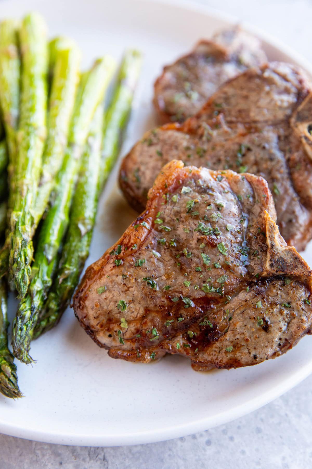 White plate of air fryer pork chops with asparagus to the side.