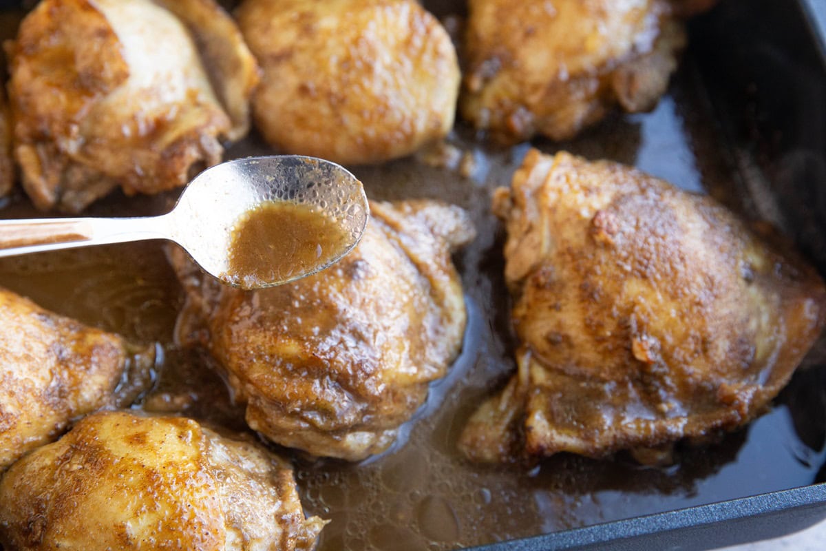 Spoon basting chicken with juices from the pan.