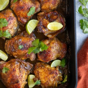 large casserole dish full of baked jerk chicken with lime wedges and cilantro sprinkled on top.