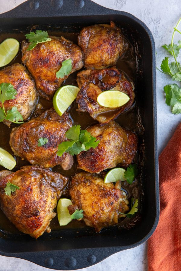 large casserole dish full of baked jerk chicken with lime wedges and cilantro sprinkled on top.