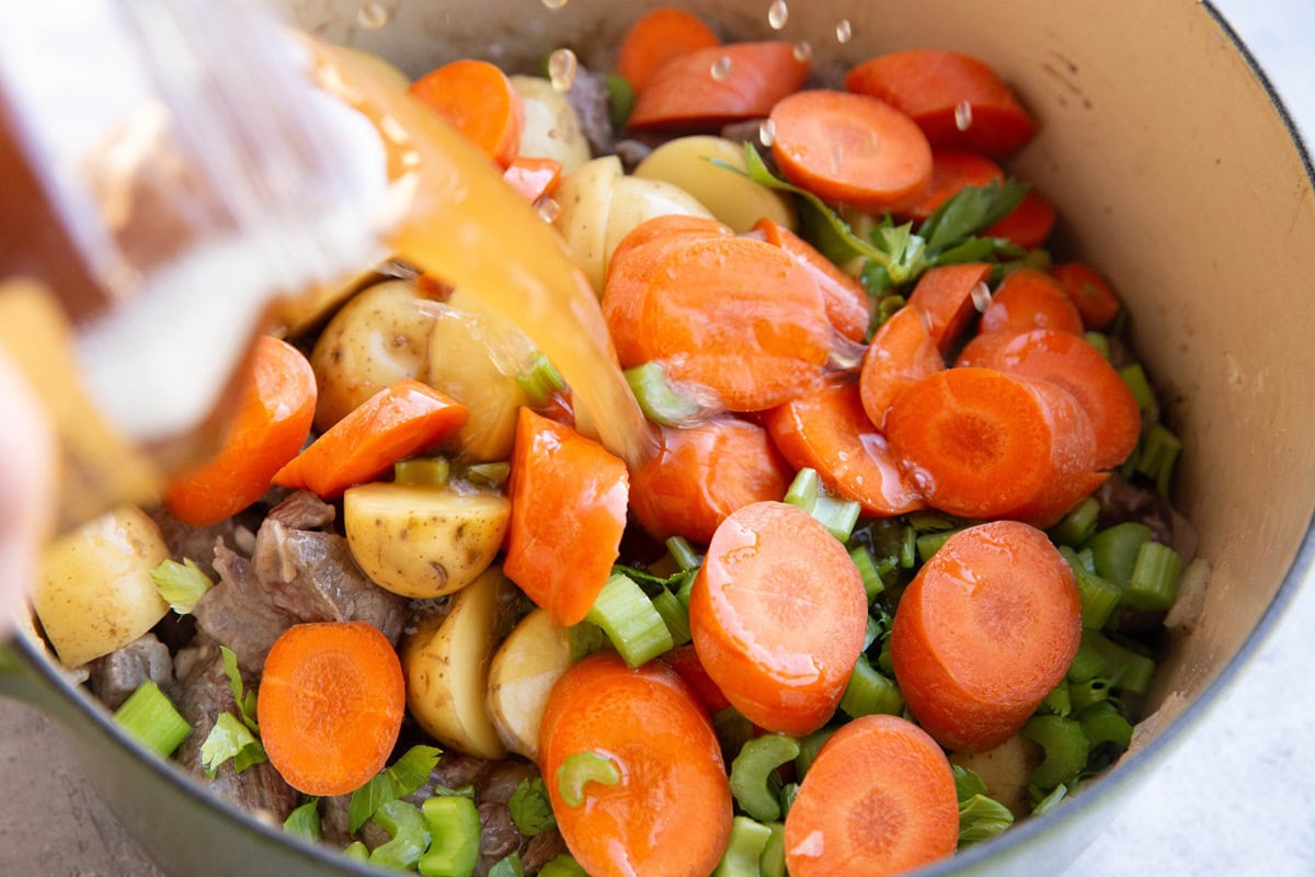 Pouring beef broth into a large pot with the beef stew ingredients.