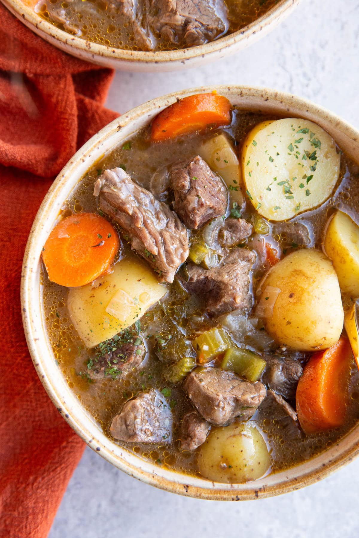 Two bowls of beef stew with a red napkin to the side.