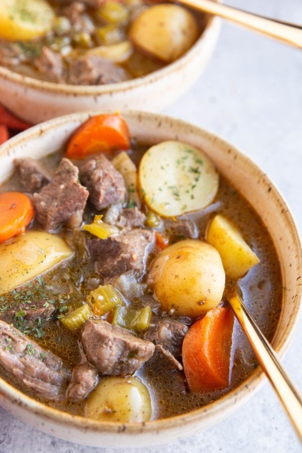 Two bowls of beef stew with potatoes and carrots.