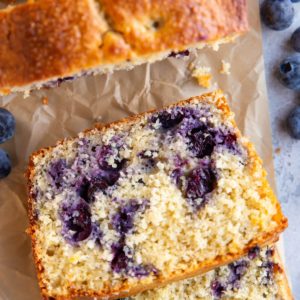 Lemon blueberry protein bread cut into slices on parchment paper with fresh berries all around.