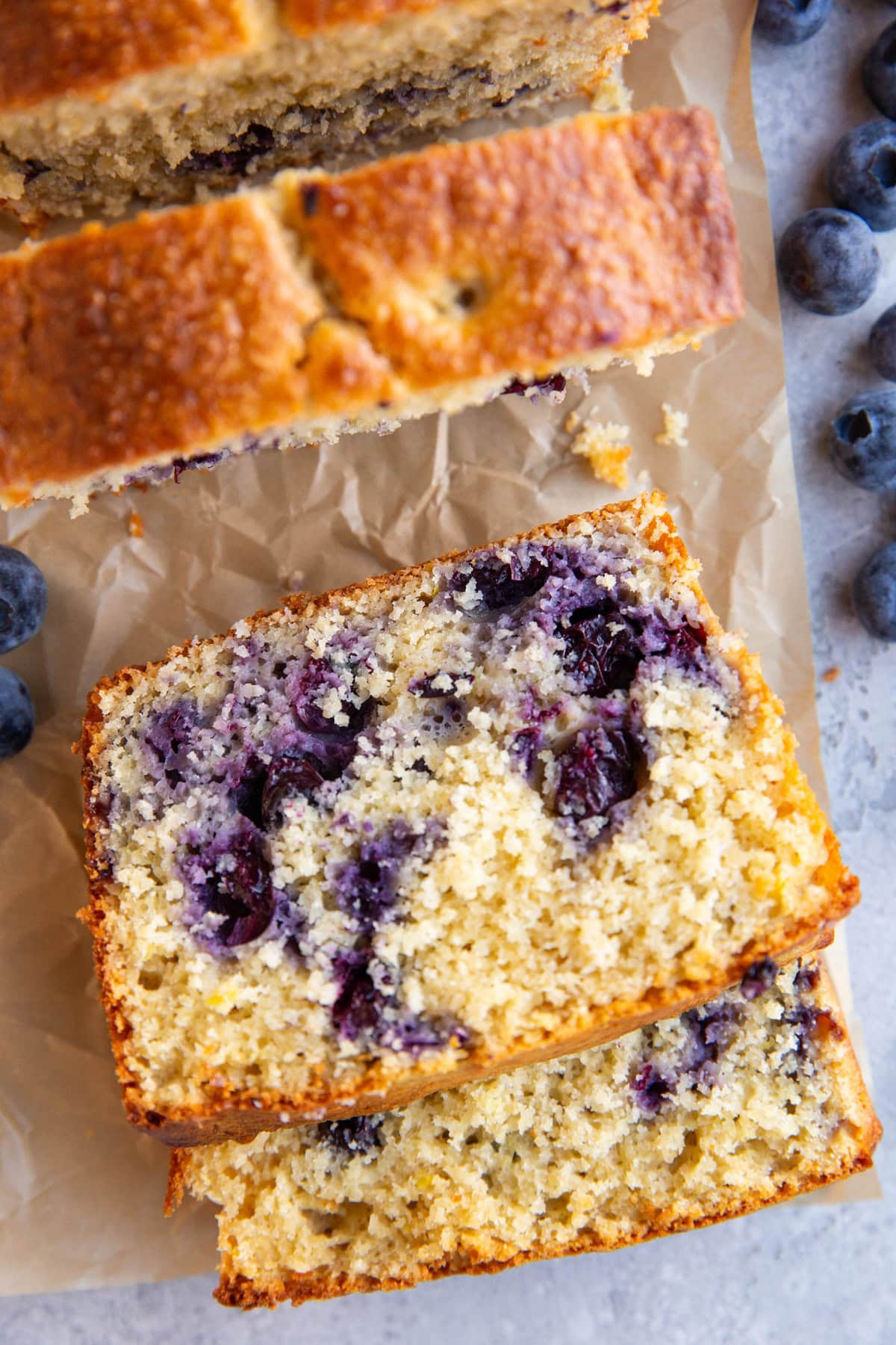 Lemon blueberry protein bread cut into slices on parchment paper with fresh berries all around.