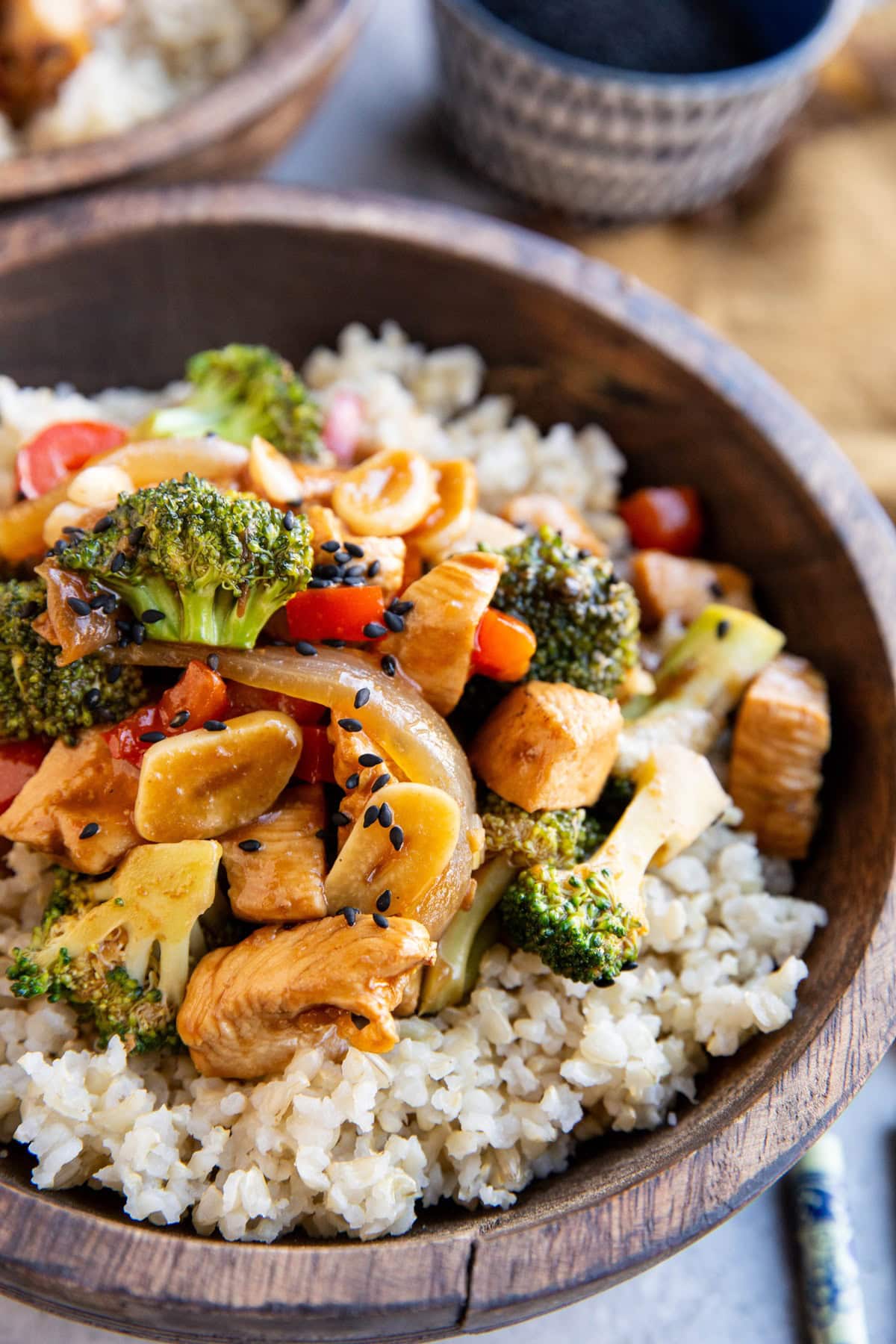 Wooden bowl of brown rice and broccoli and chicken stir fry with chop sticks to the side.