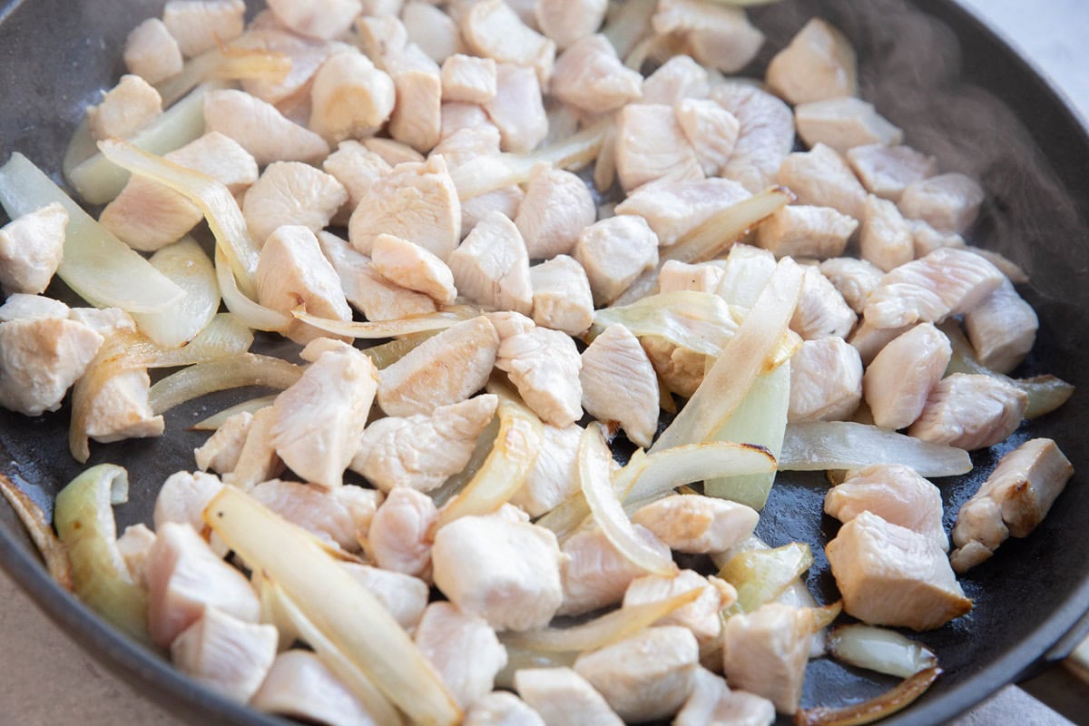 Chicken and onions cooking in a skillet.