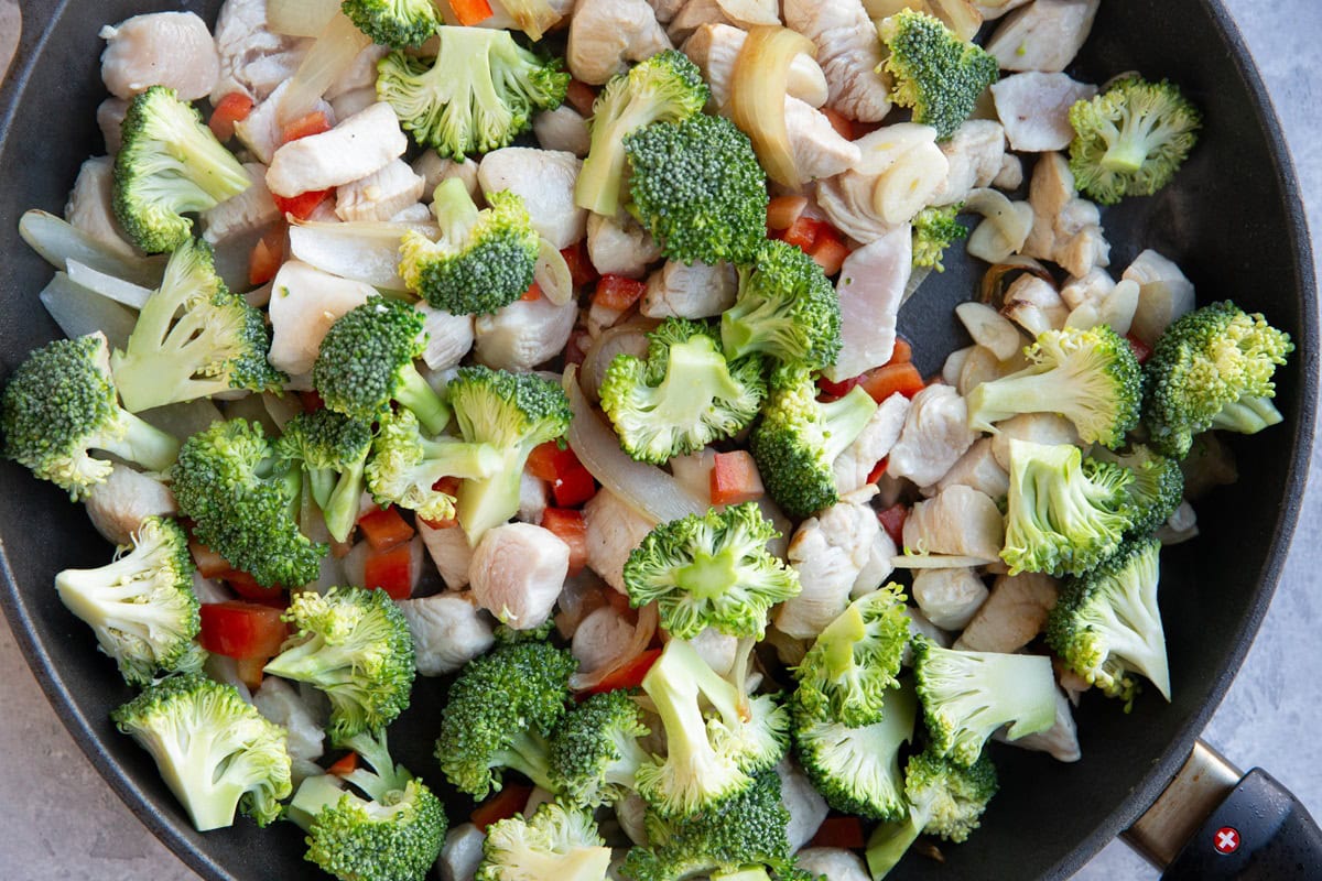 Broccoli, bell pepper, chicken, and onions cooking in a skillet.