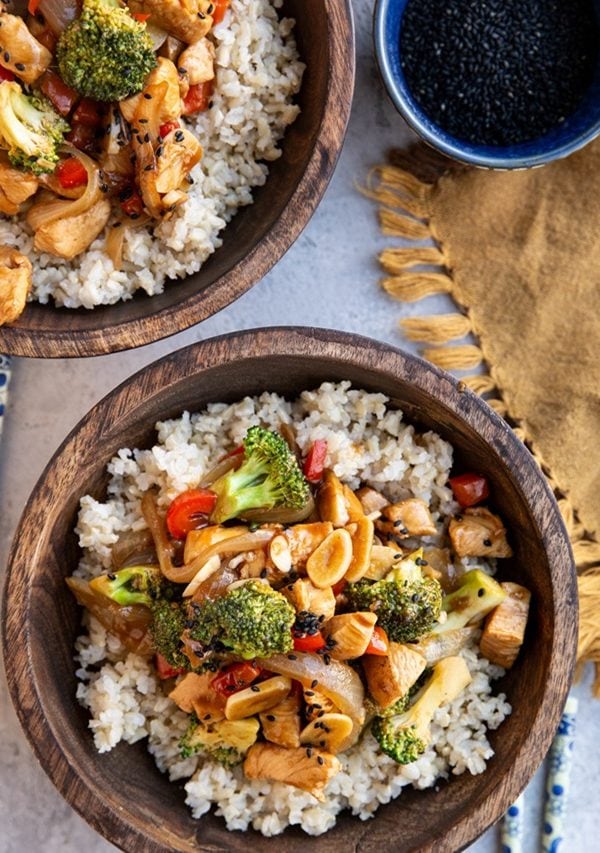 Two wooden bowls full of chicken stir fry with chop sticks to the side.