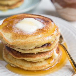 Stack of coconut flour pancakes on a plate with melted butter on top, ready to eat.