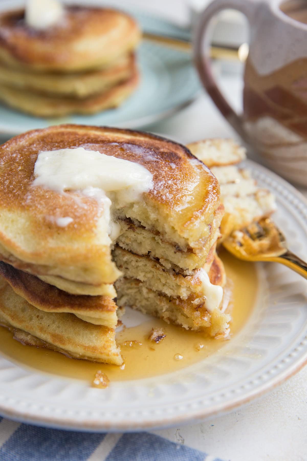 Stack of coconut flour pancakes on a plate with melted butter on top and a bite taken out of the pancakes exposing the middle.