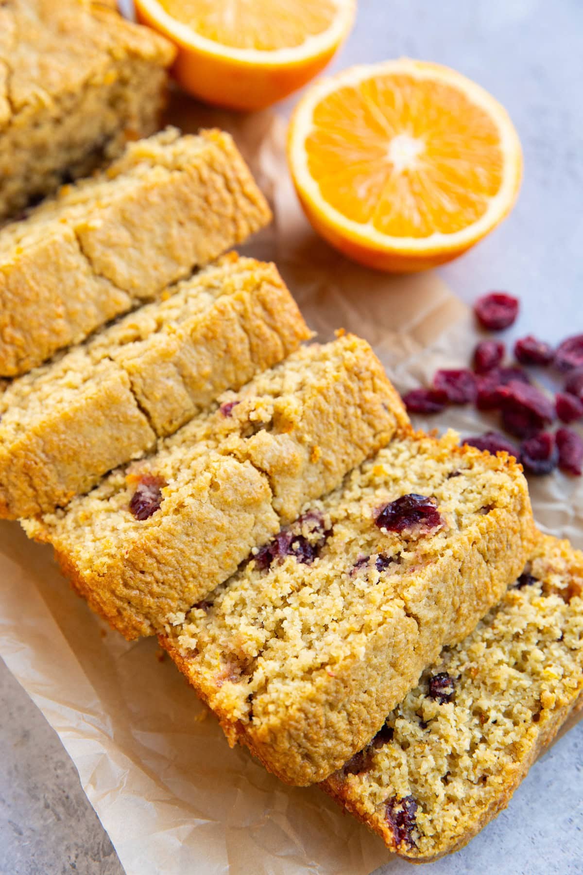 Loaf of cranberry orange bread cut into slices with a fresh orange and dried cranberries in the background.