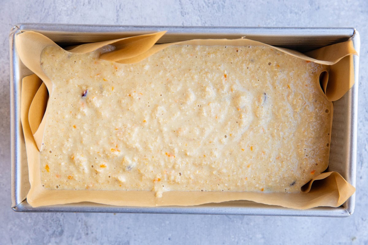 Loaf pan with cranberry orange batter inside to make bread