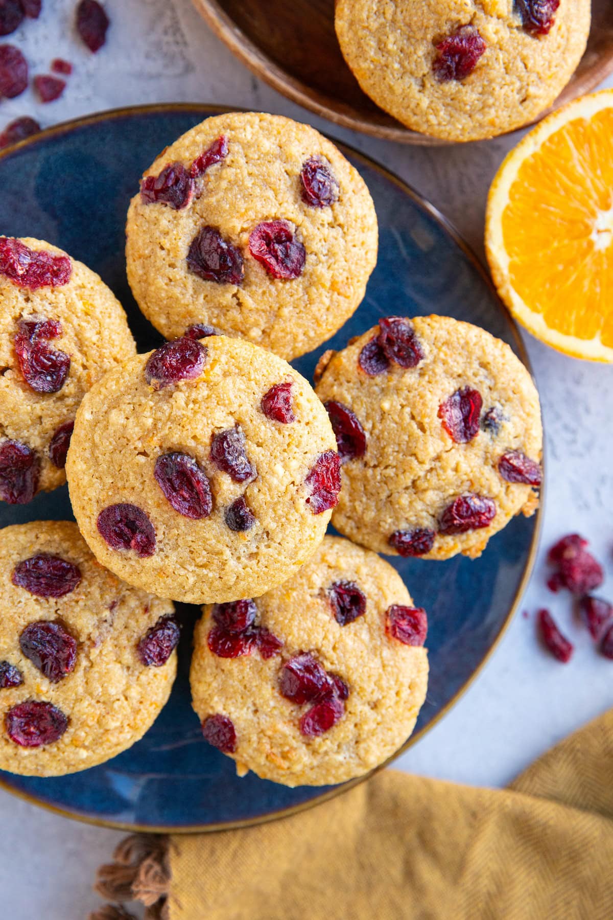 Blue plate with cranberry orange muffins on top. A sprinkle of cranberries to the side and a fresh orange.