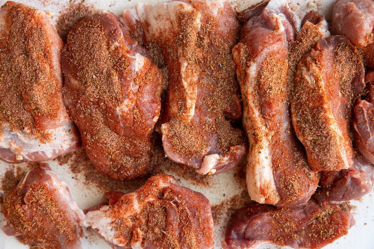 Chunks of pork roast sprinkled with dry rub on a cutting board.