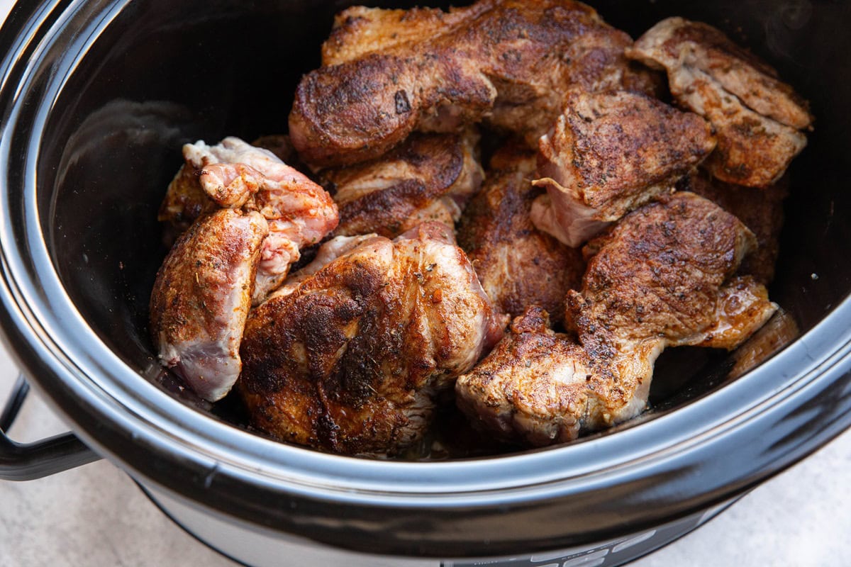 Crock pot full of seared pork meat and onions to make carnitas.