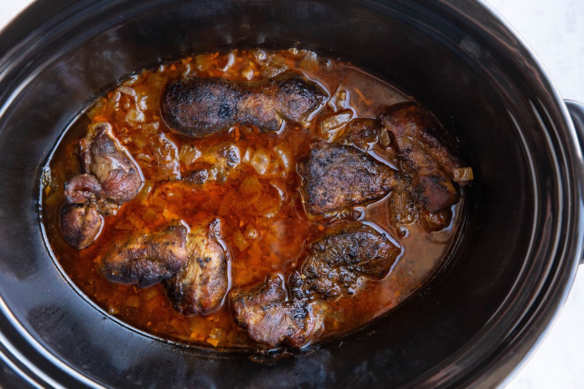 Slow cooker full of seared meat and juices for carnitas.