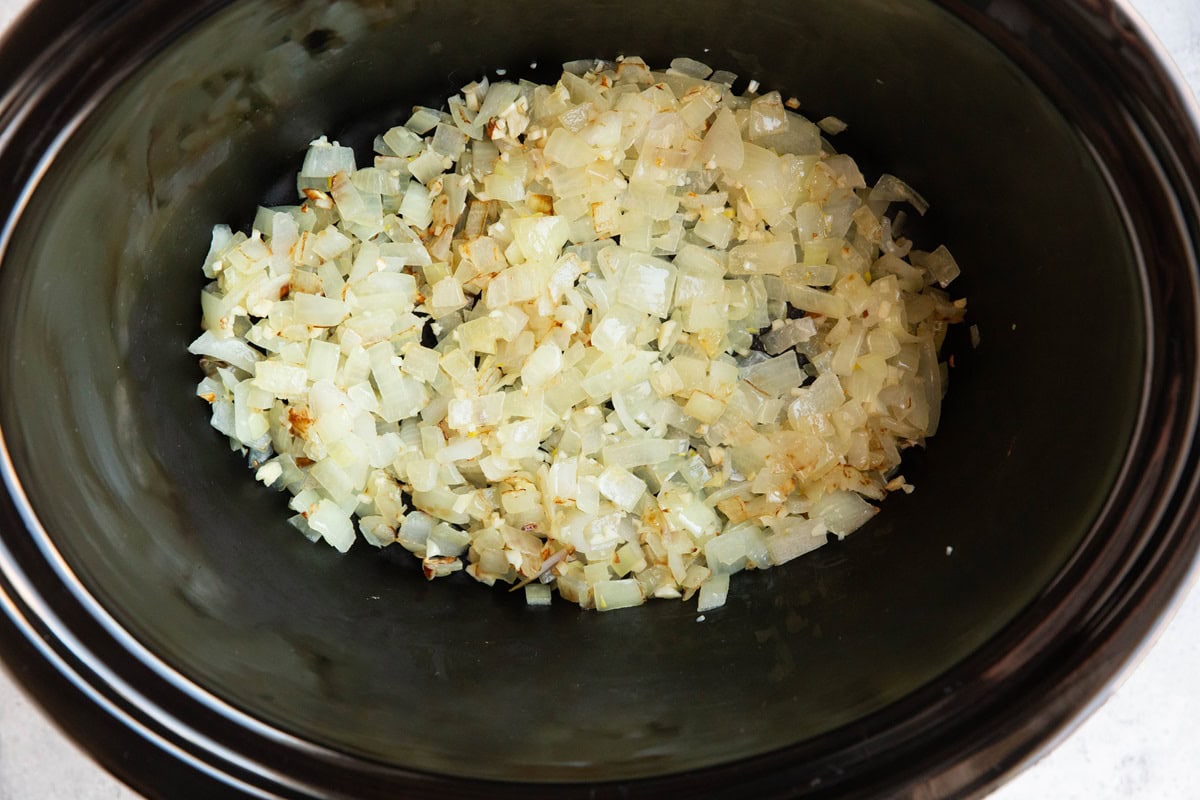 Crock pot with sauteed onions and garlic inside.