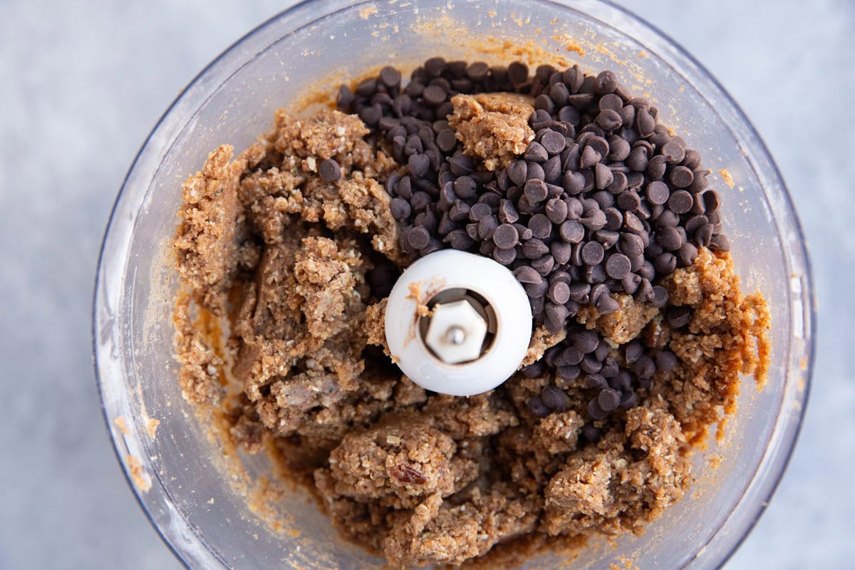 Energy bite mixture in a food processor with chocolate chips on top, ready to be mixed in.