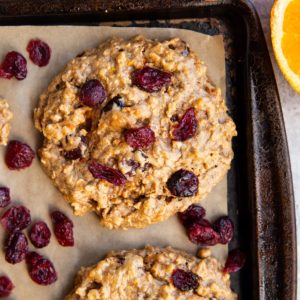 Baking sheet with cranberry orange cookies on top and a fresh orange sliced to the side.