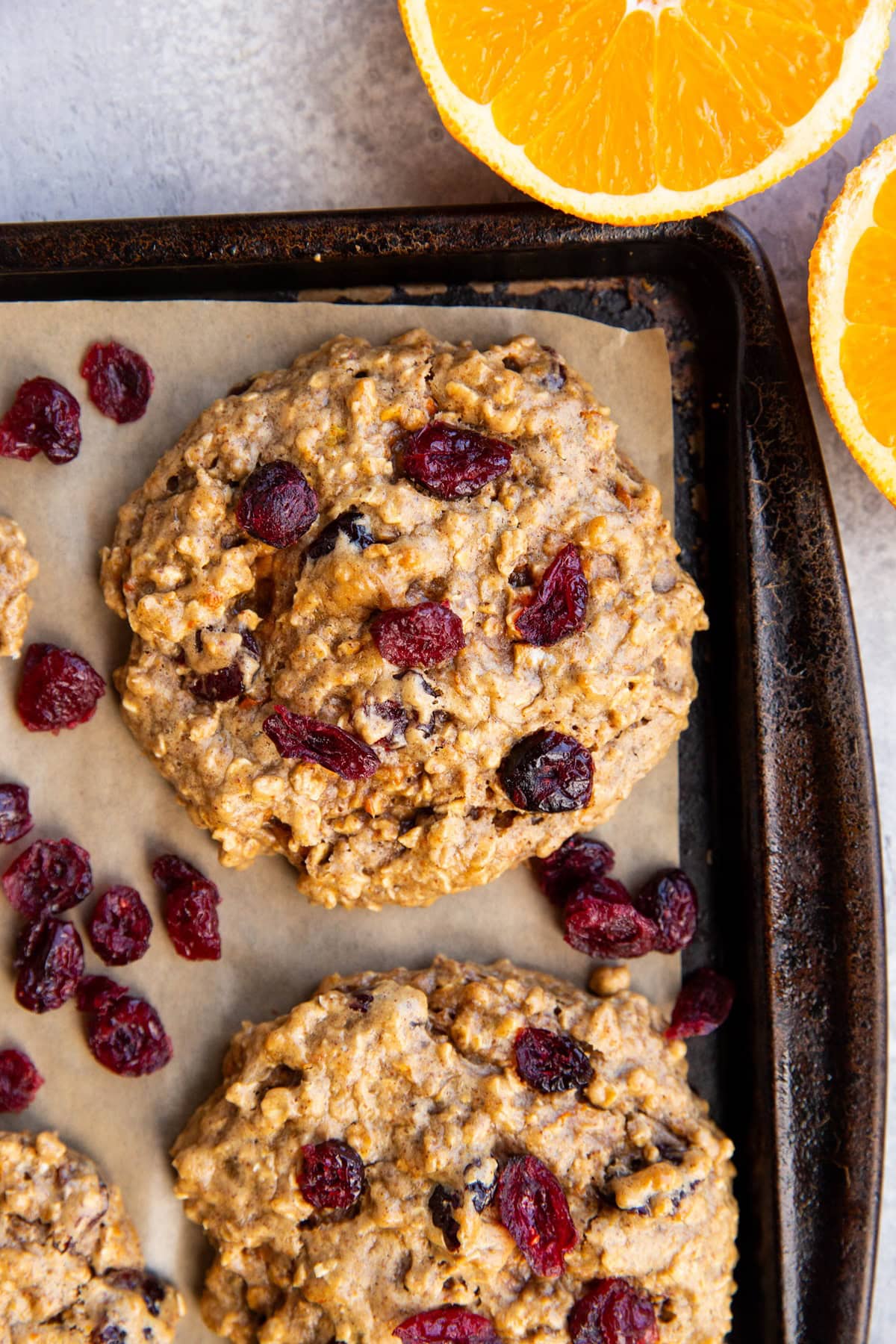 Baking sheet with cranberry orange cookies on top and a fresh orange sliced to the side.