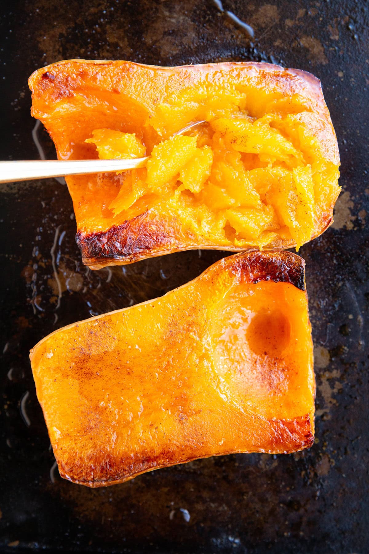 Butternut squash halves on a sheet pan, fresh out of the oven, with a spoon digging into one of the halves.