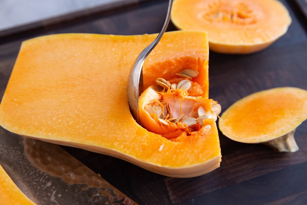 Spoon scooping the seeds out of a butternut squash.