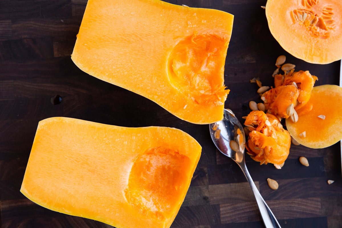 Butternut squash halves on a wooden cutting board with the seeds scooped out.