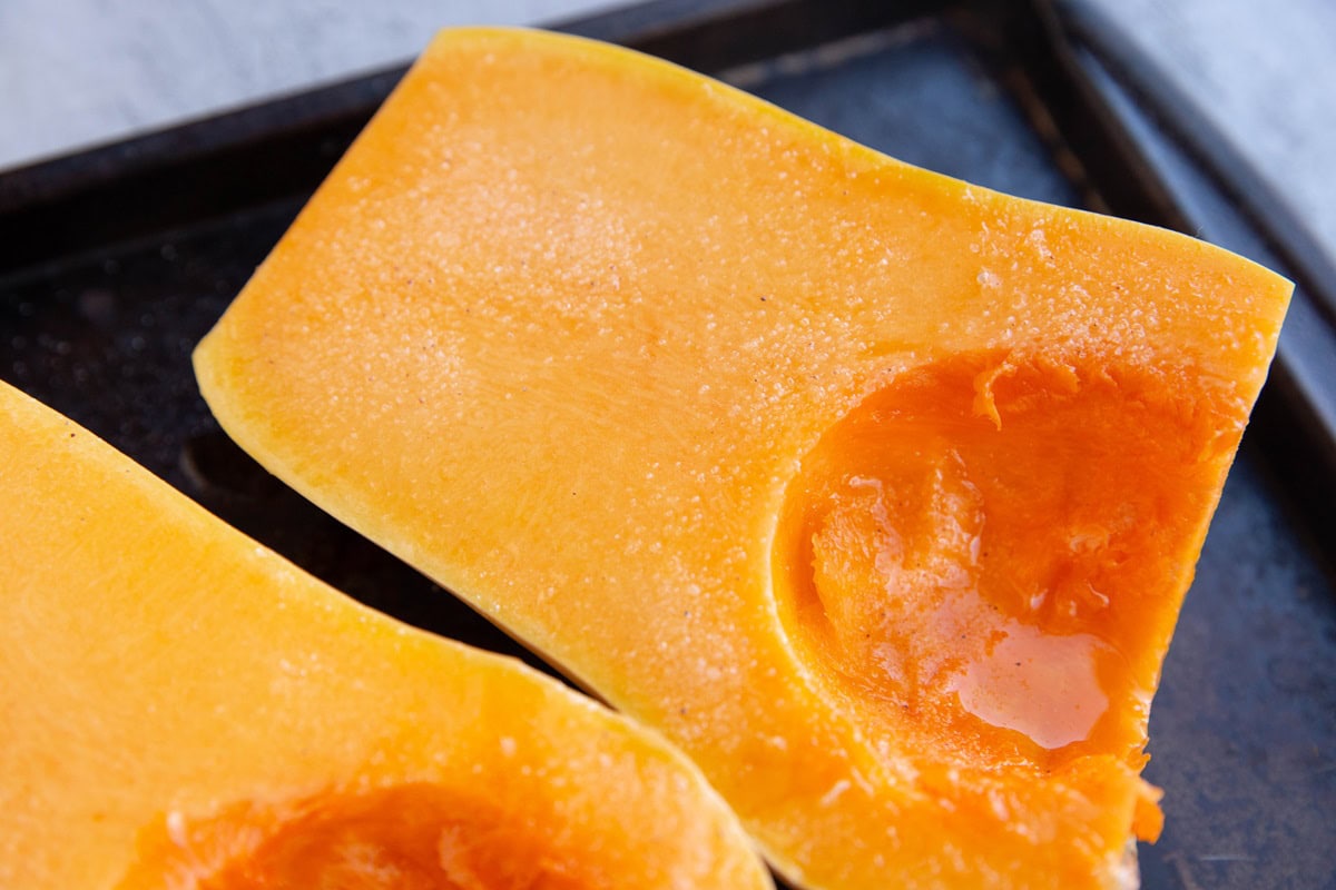 Butternut squash halves coated with oil and sprinkled with sea salt, ready to be baked.