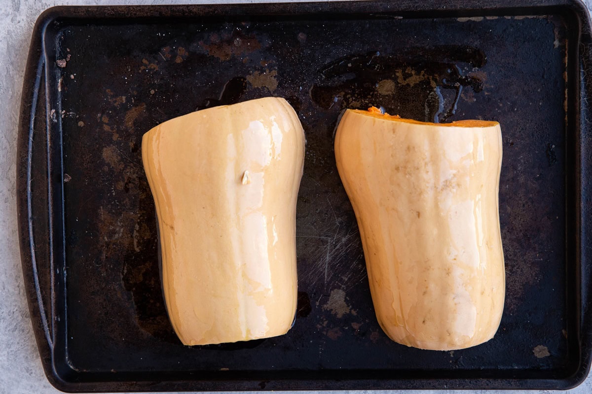 Baking sheet with butternut squash sliced in half, cut side down ready to roast.