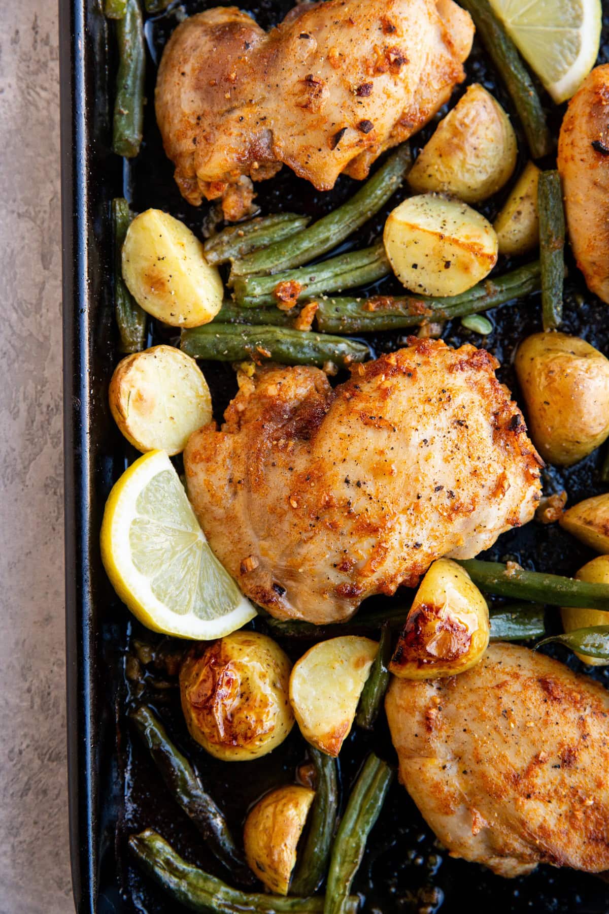 Baking sheet of chicken, potatoes, and green beans with lemon slices.