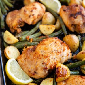 Baking sheet full of lemon chicken and vegetables.