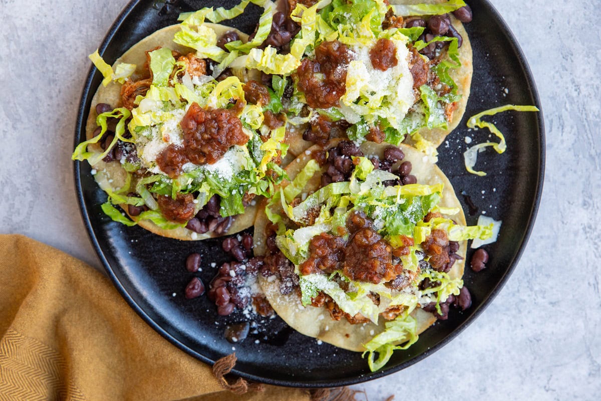 Black plate full of three chicken tostadas, ready to eat.