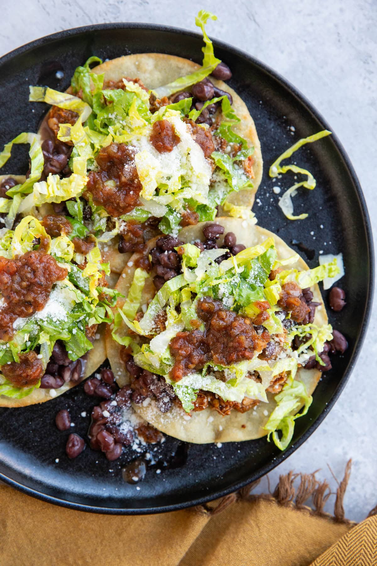 Black plate full of chicken tostadas with toppings.