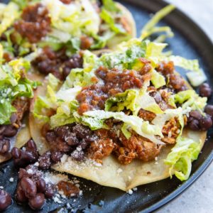 Tostada with shredded chicken and beans on a plate.