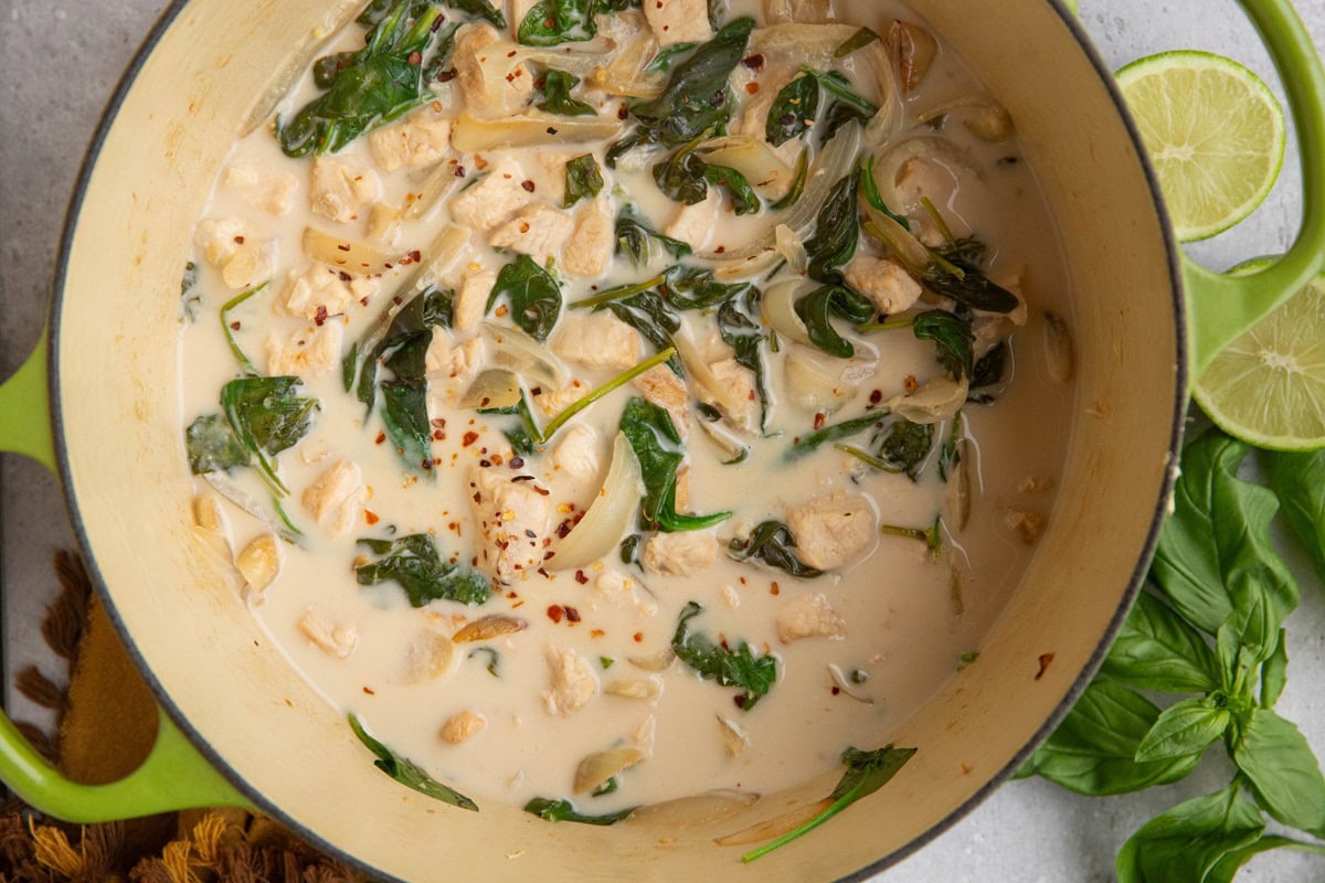 large pot full of cooked coconut chicken with basil, spinach, and a sprinkle of red pepper flakes.