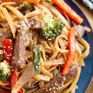 Blue plate with beefy noodles and veggies with chopsticks to the sides.