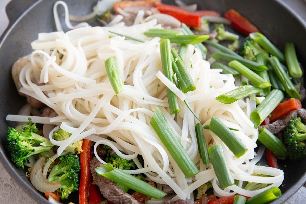 Large skillet with beef, vegetables, noodles, and green onions to make stir fry noodles.