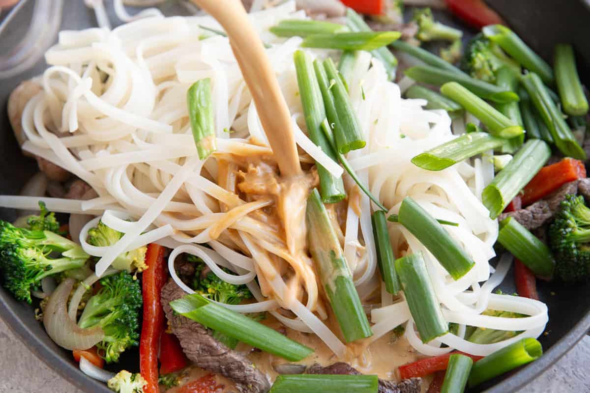 Pouring sauce into the skillet with the noodles, beef, and veggies.