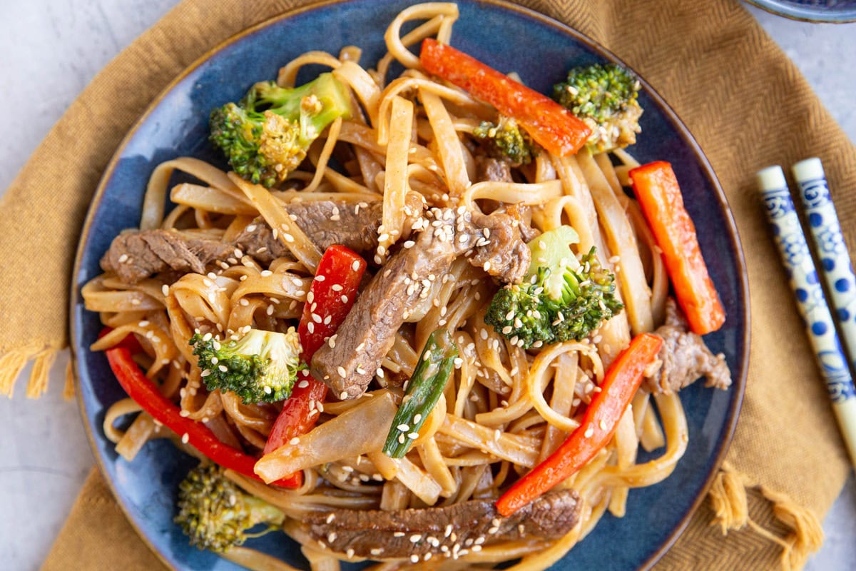 Blue plate with stir fry noodles on top. Chop sticks to the side and a napkin.