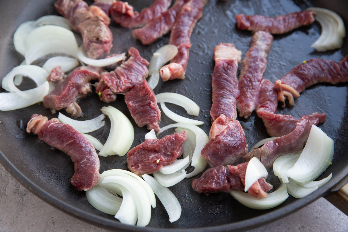 Sliced beef and onions browning in a skillet.