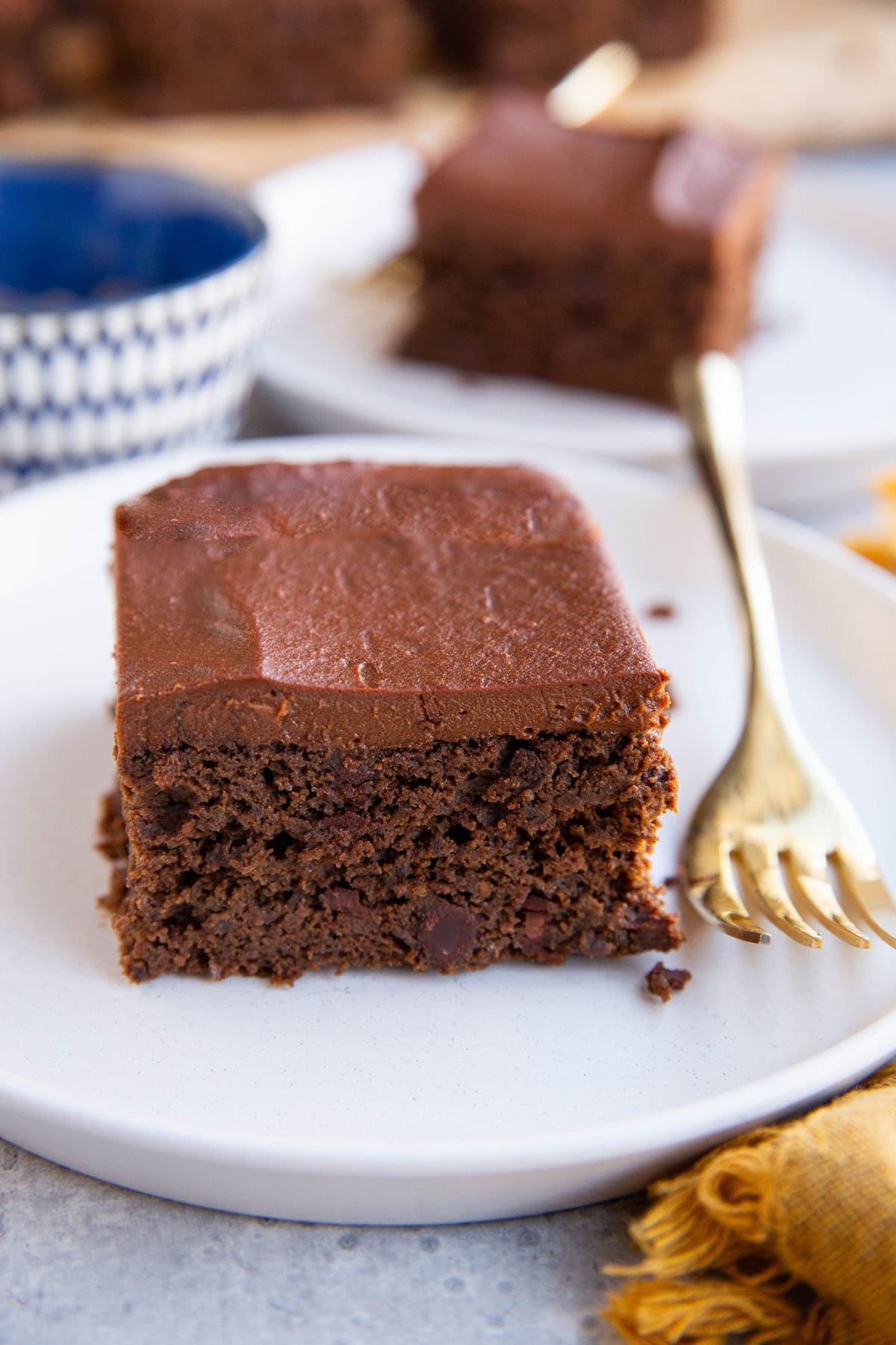 Two slices of black bean cake on two white plates with a golden napkin and the rest of the cake in the background.