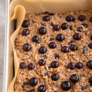 Baking dish with blueberry oatmeal bars fresh out of the oven and a bowl of fresh blueberries in the background.